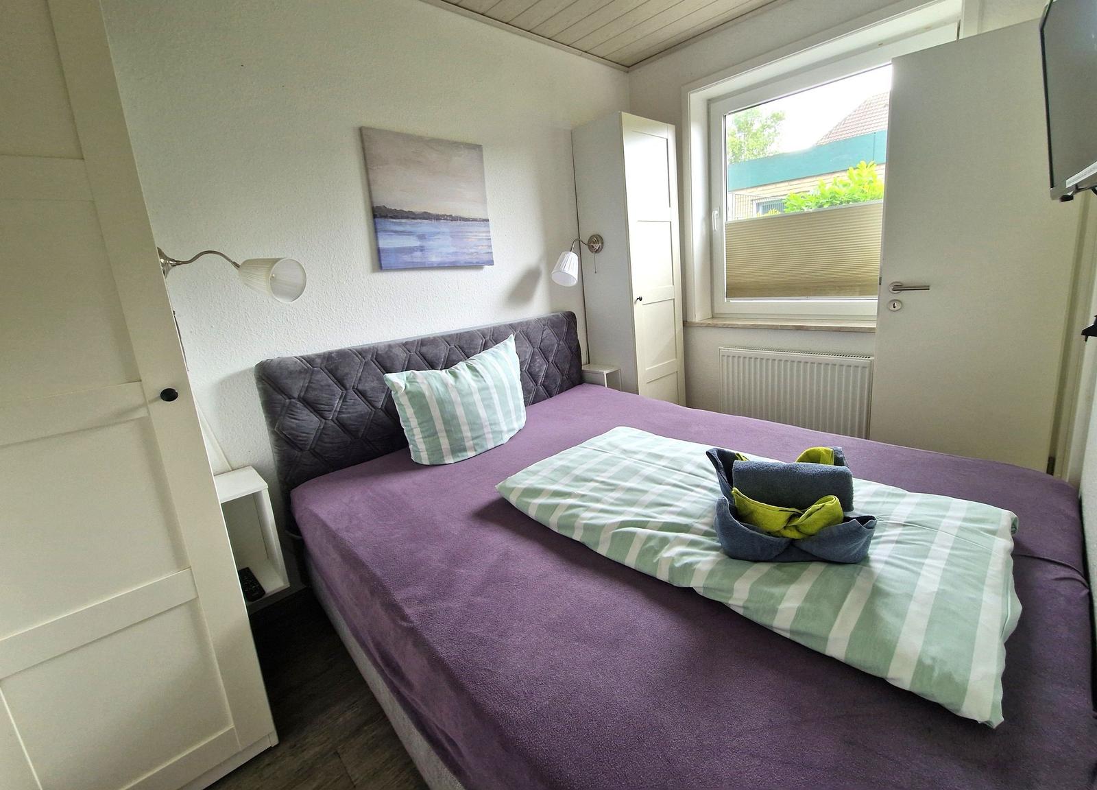 Schlafzimmer mit Bett, Wandbild und Fenster. Handtuch auf Bett.