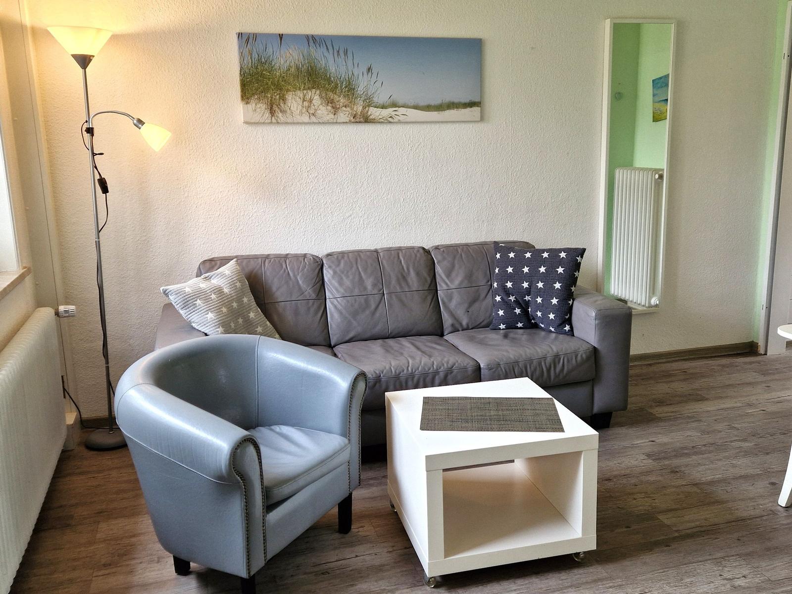Ein Wohnzimmer mit grauem Sofa, blauem Sessel und weißem Couchtisch.