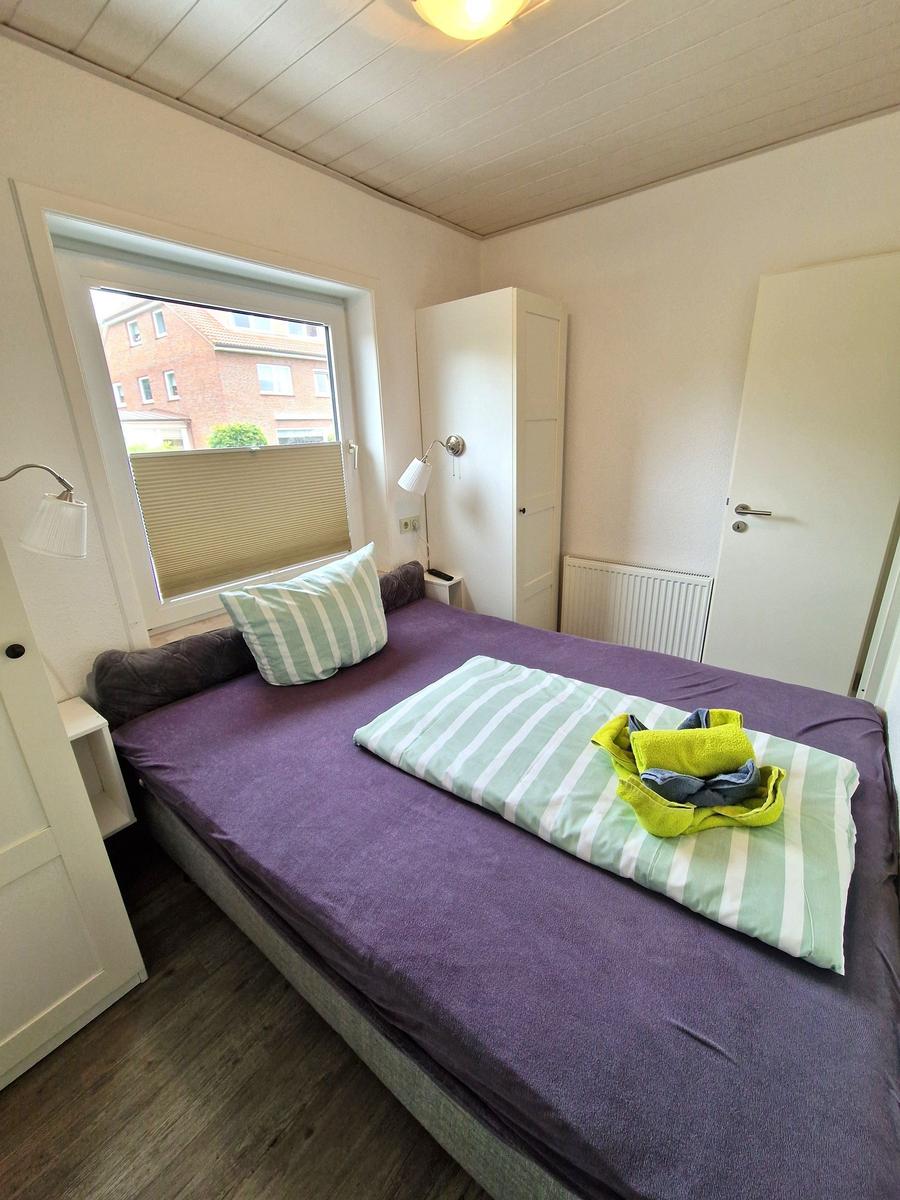 Schlafzimmer mit Bett, Fenster und Kleiderschrank. Auf dem Bett liegen Handtücher.