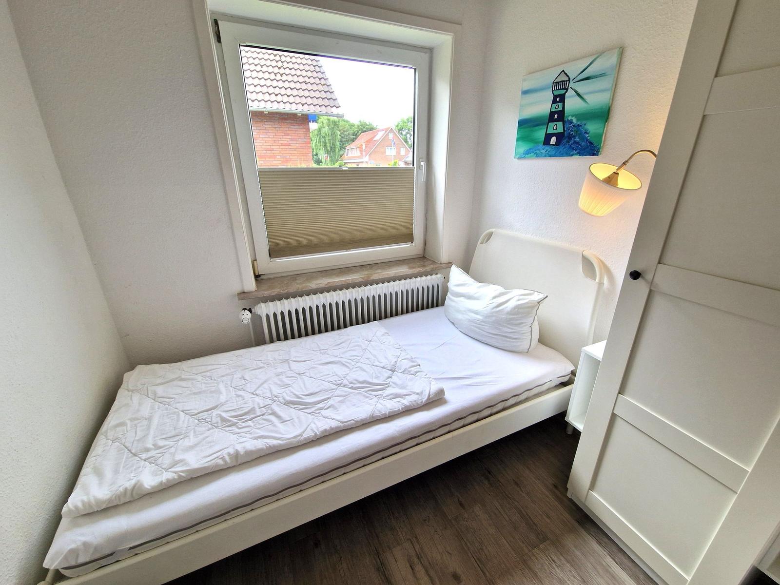 Ein Schlafzimmer mit weißem Bett, Fenster und Wandbild mit Leuchte.