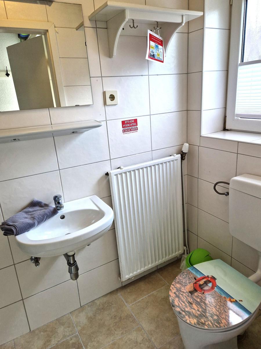 Badezimmer mit Waschbecken, Spiegel, Toilette und Heizkörper an der Wand.