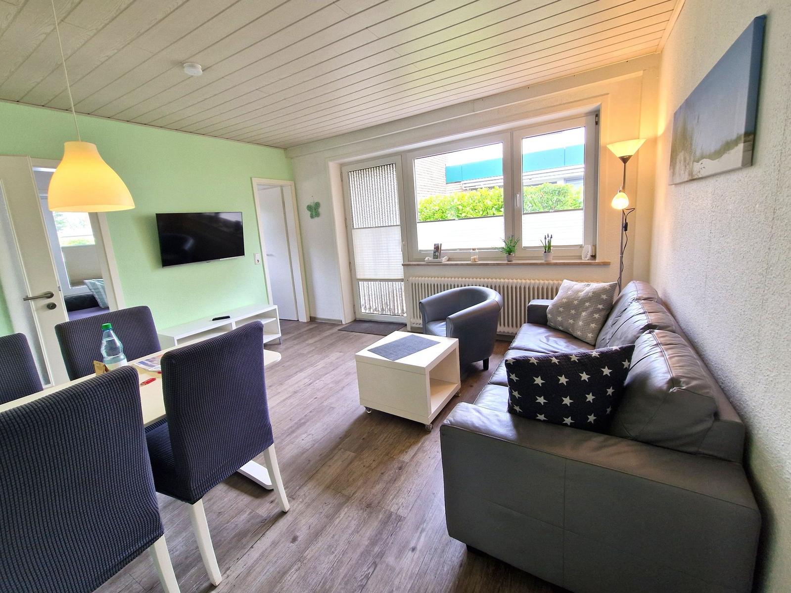 Wohn- und Essbereich mit Sofa, Tisch, Stühlen und TV an der Wand.