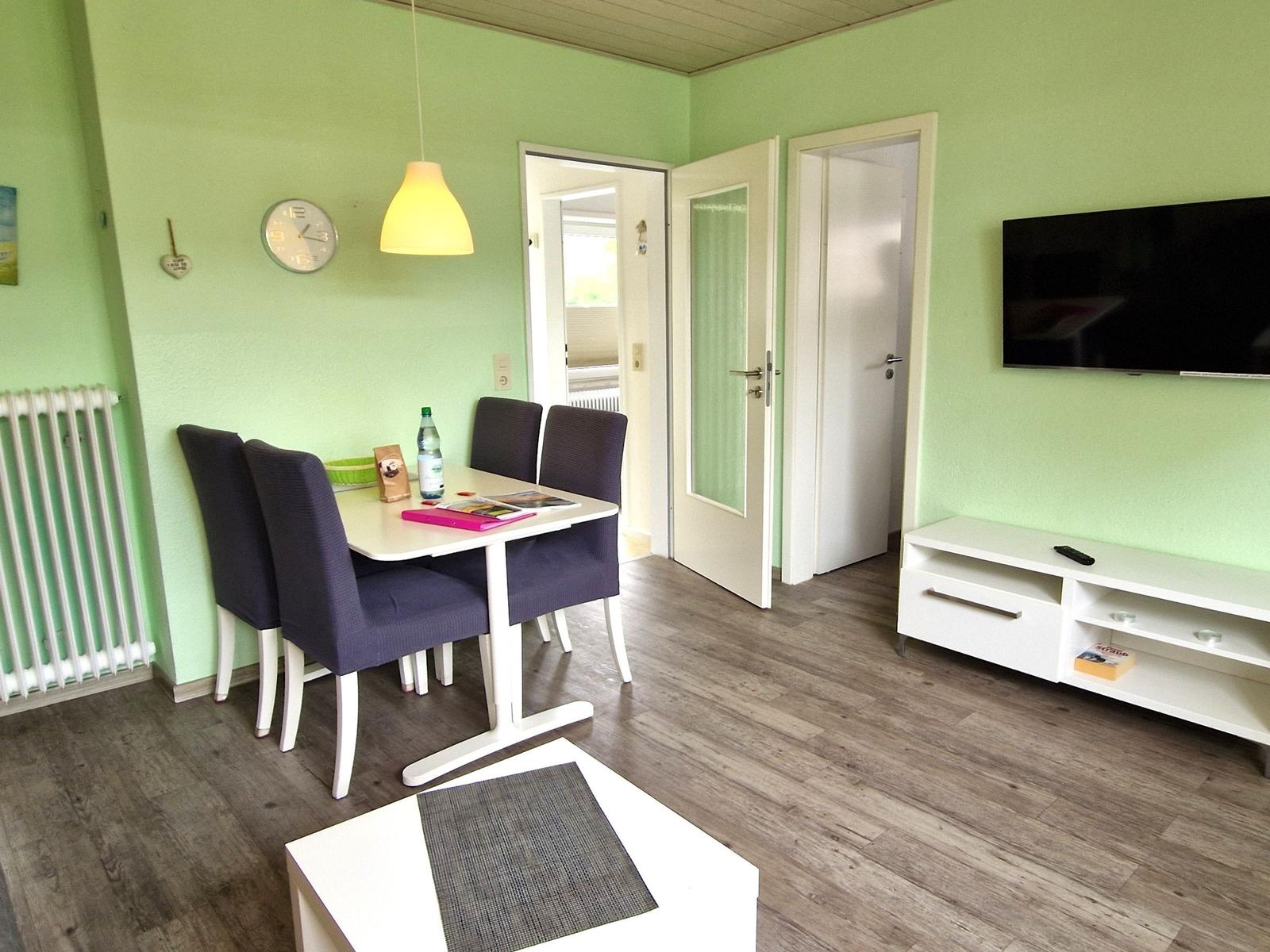 Essbereich mit Tisch, Stühlen und Fernseher an der Wand.