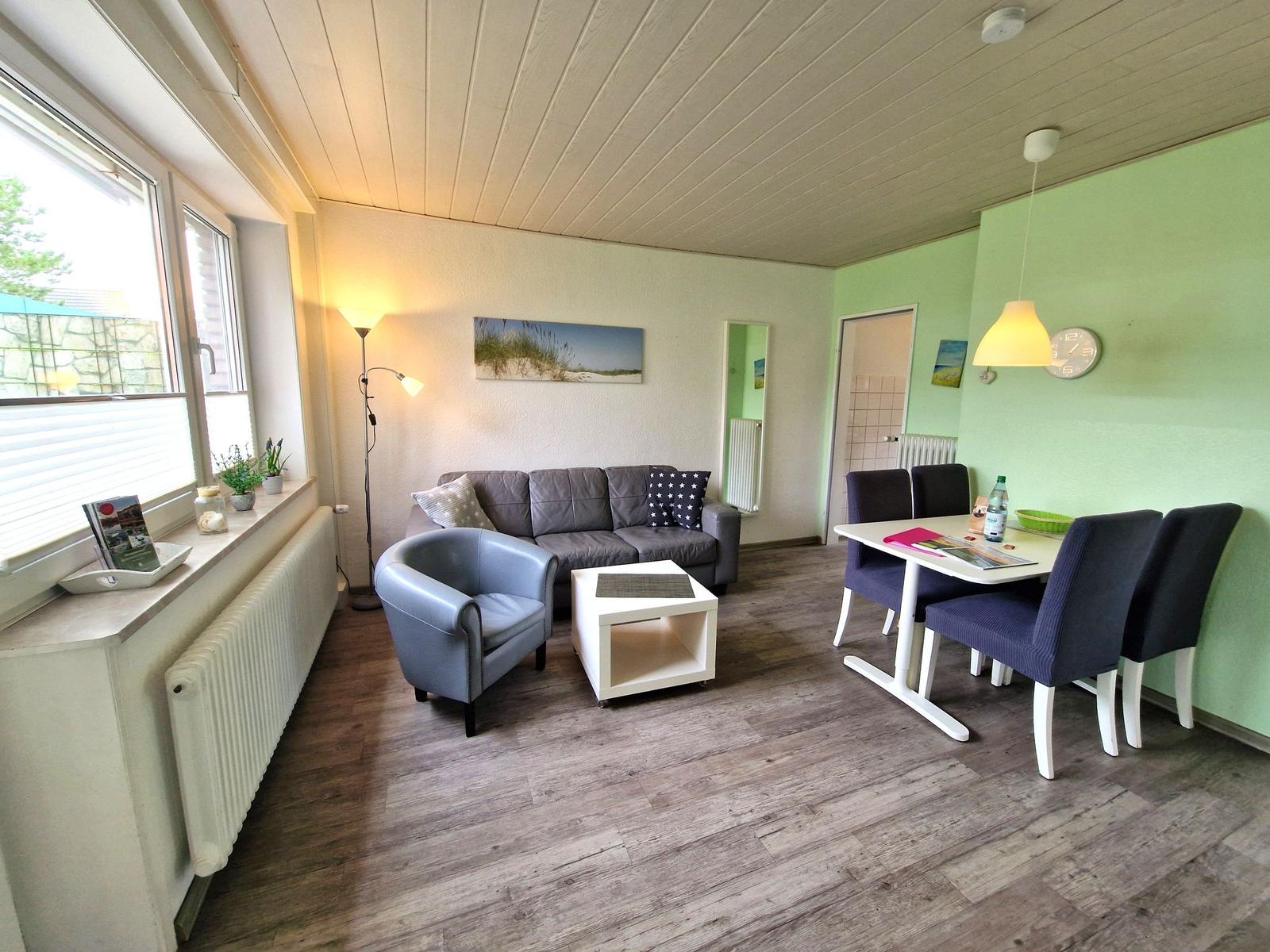 Wohn- und Essbereich mit Sofa, Stuhl und Tisch. Wandfarbe grün, Holzboden und Fenster.