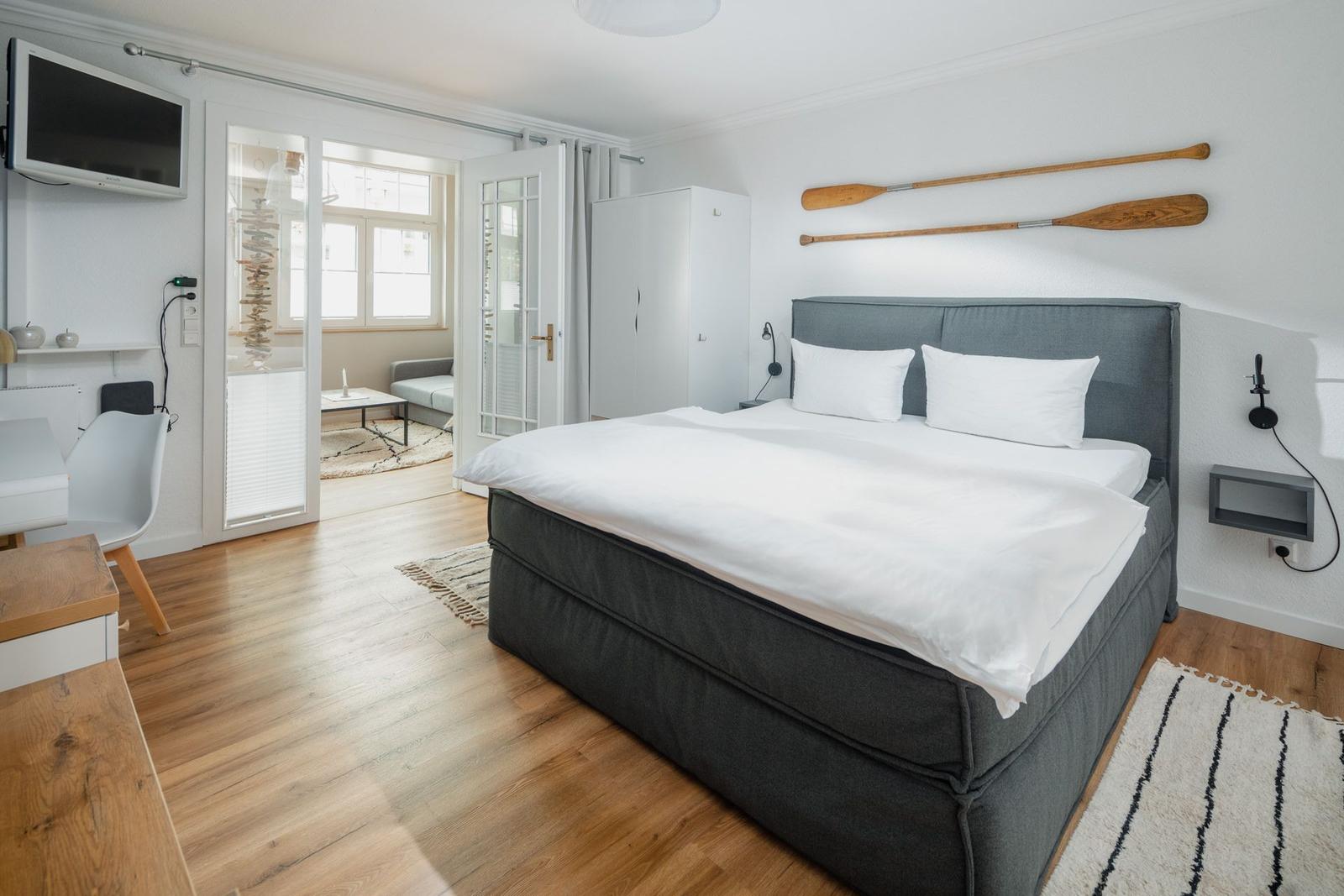 Schlafzimmer mit Bett, Fernseher und Blick in Wohnbereich.