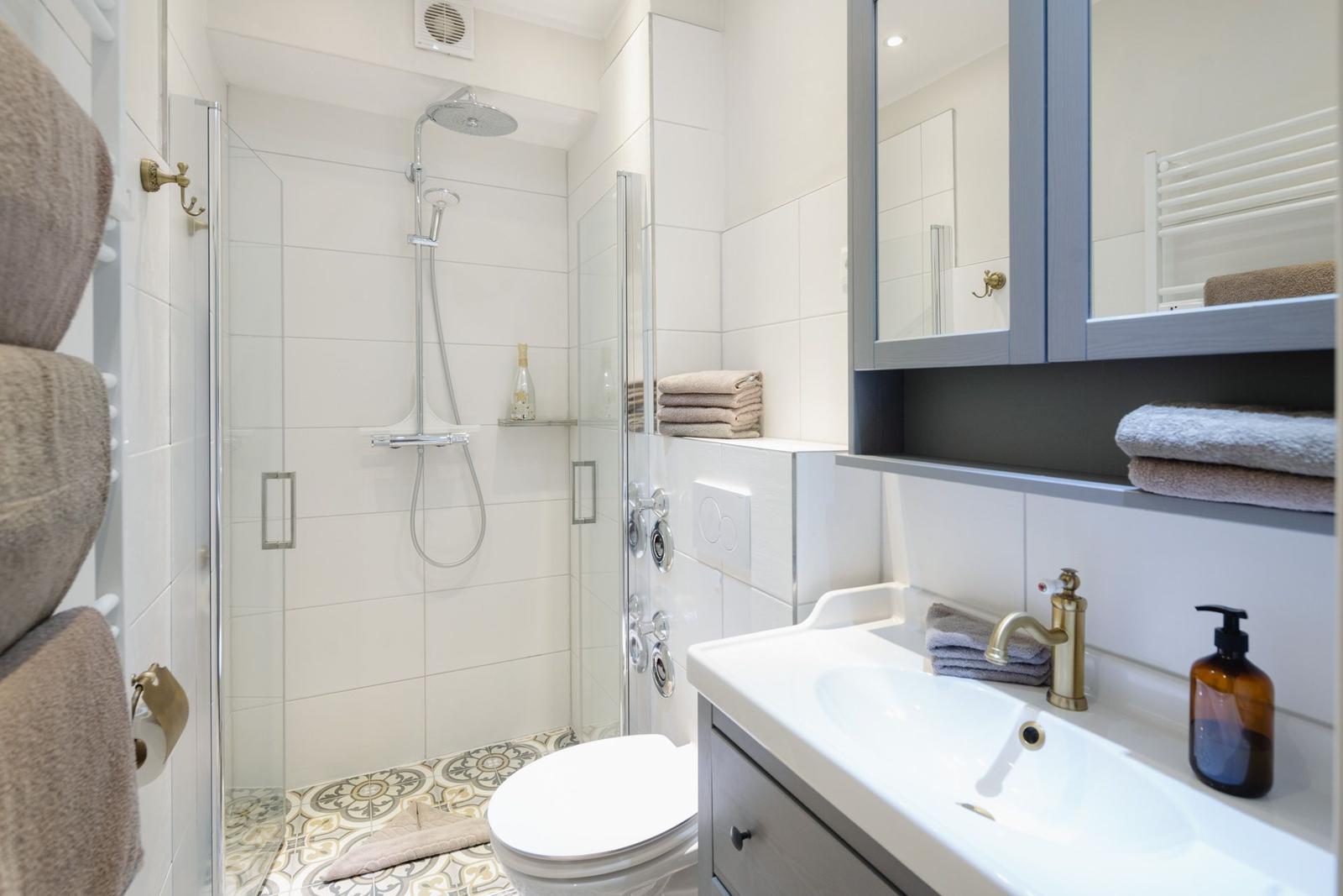Bad mit Dusche, Waschbecken und Spiegelschrank. Handtuchhalter und Fliesenboden.