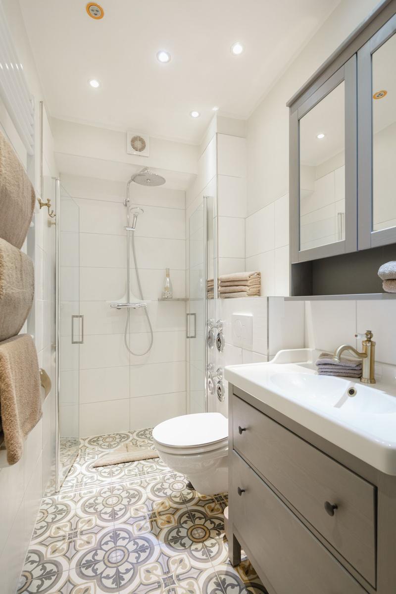 Badezimmer mit Dusche, Waschbecken und Toilette. Bodenfliesen mit Muster.