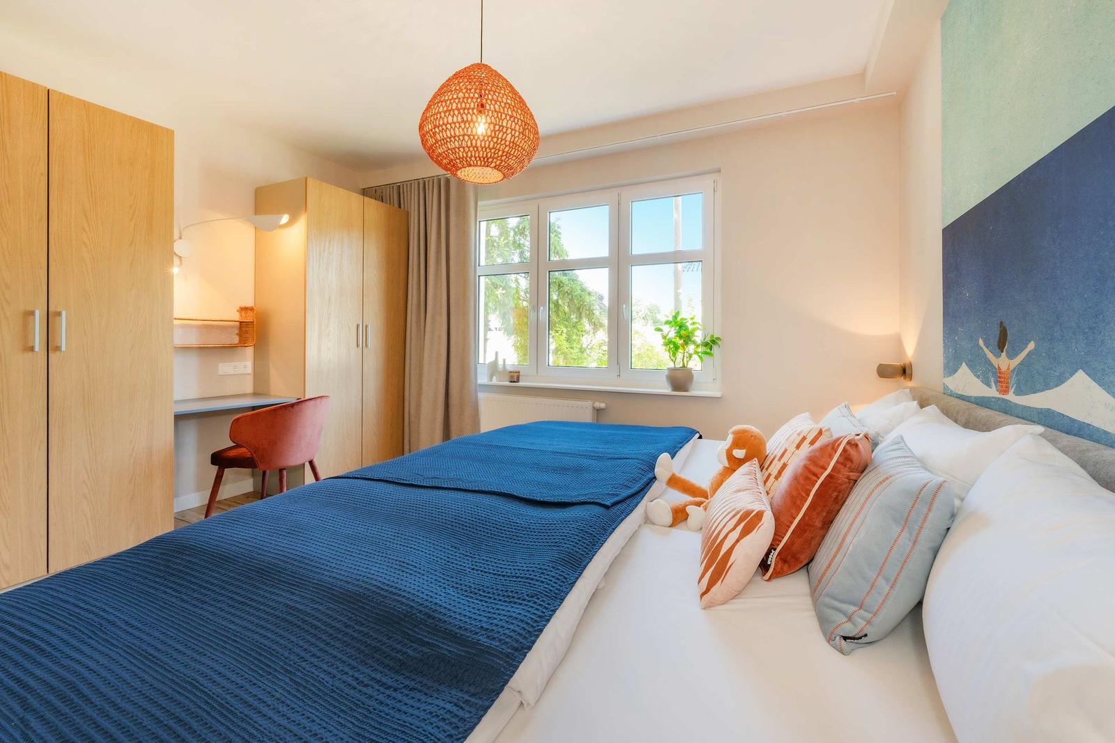 Schlafzimmer mit Bett, Schreibtisch und Fenster. Wandbild und Deckenleuchte.