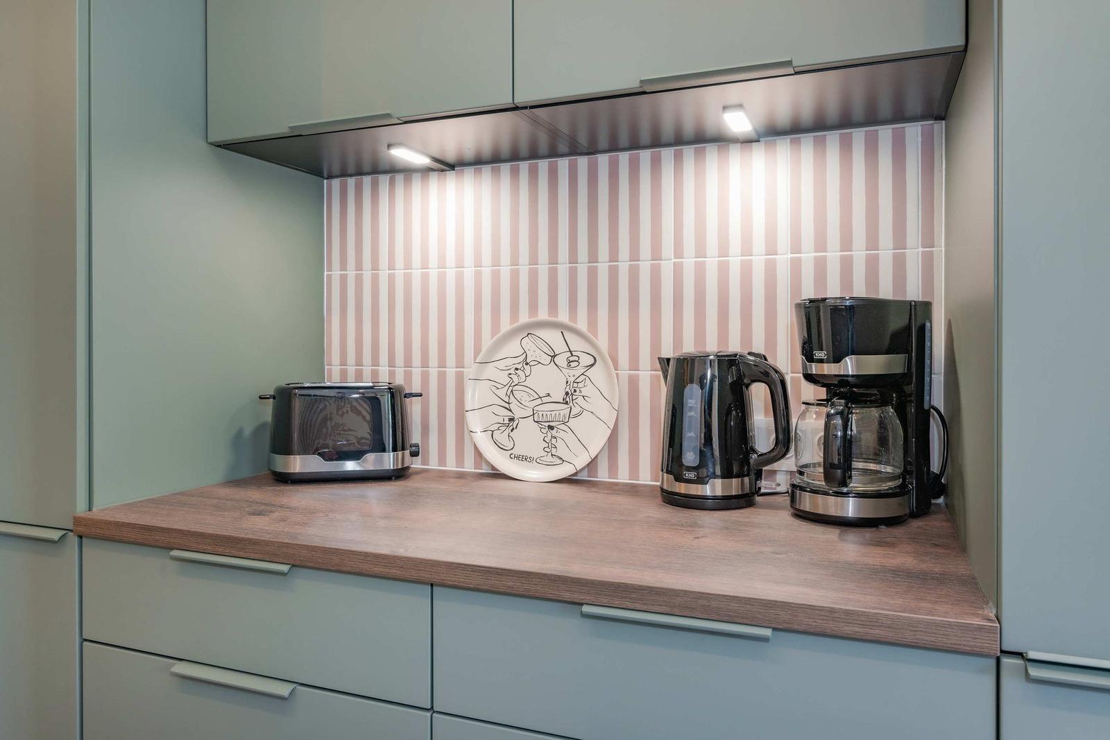 Küchenzeile mit Toaster, Kaffeemaschine und Kanne auf Holzoberfläche.