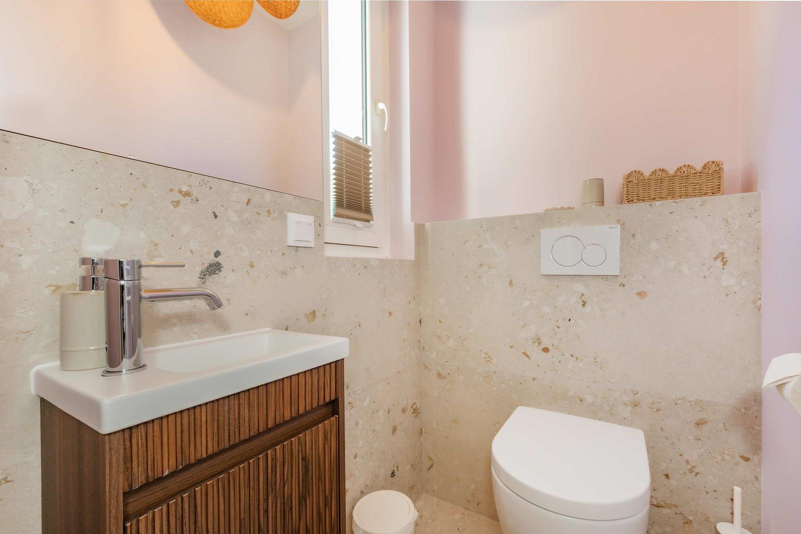 Badezimmer mit Waschbecken, Toilette und Fenster. Wandverkleidung aus Terrazzo.