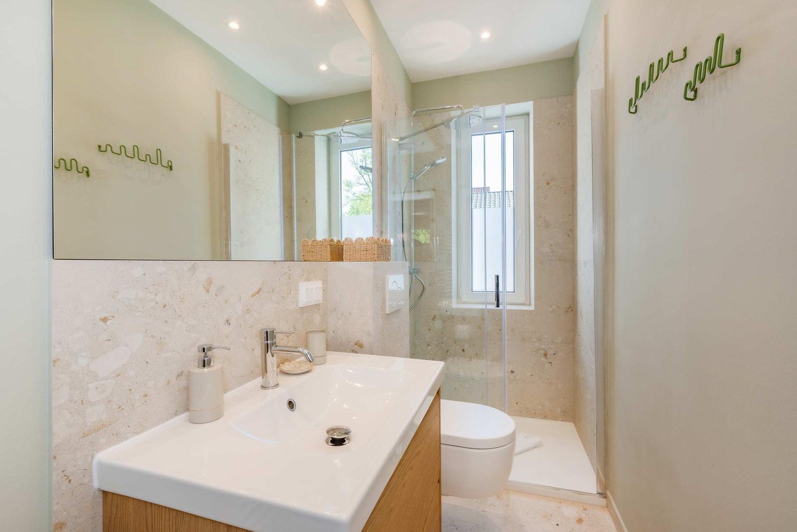 Badezimmer mit Dusche, Waschbecken und Toilette. Wandverkleidung aus Stein und grünes Dekor.