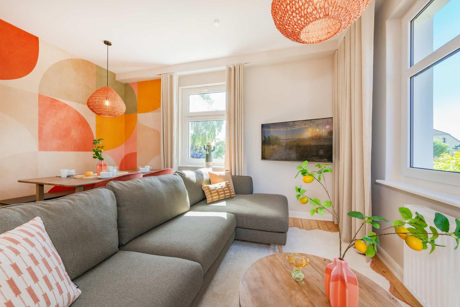 Wohnzimmer mit grauem Sofa, orangefarbenem Wandbild und runden Tischen.