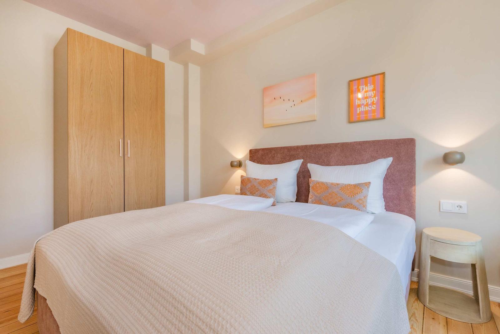 Schlafzimmer mit Bett, Kleiderschrank und Wandbildern.