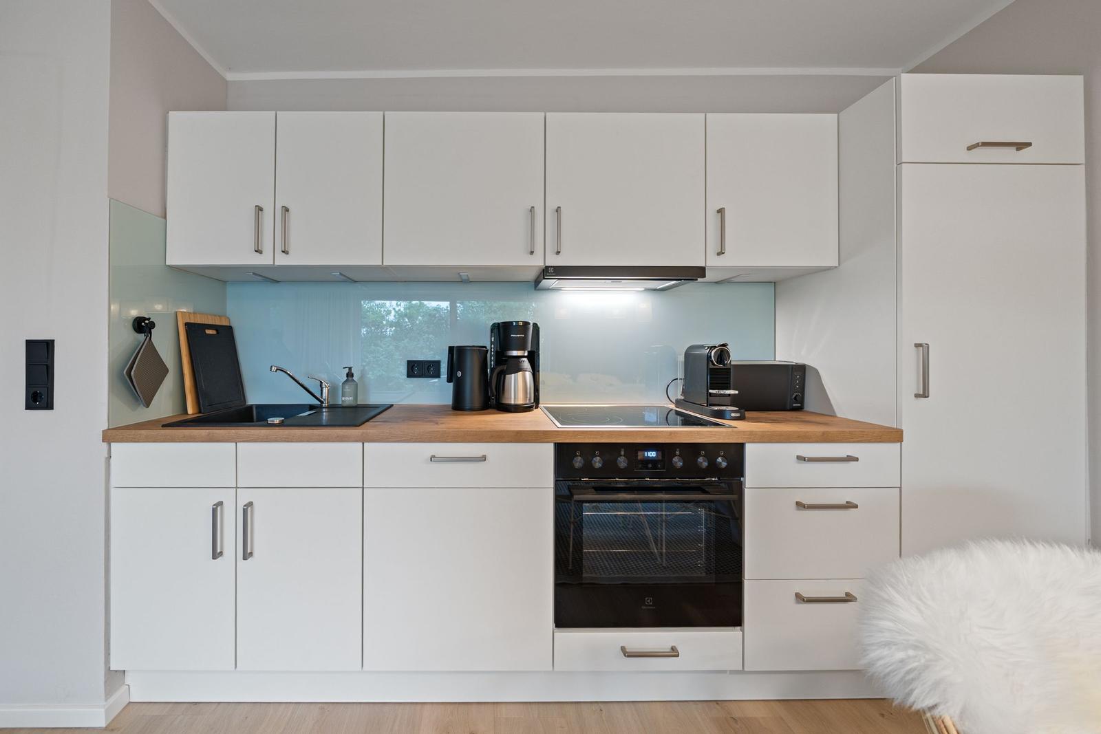 Küche mit weißen Schränken, Holzplatte, Spüle und Kochfeld.