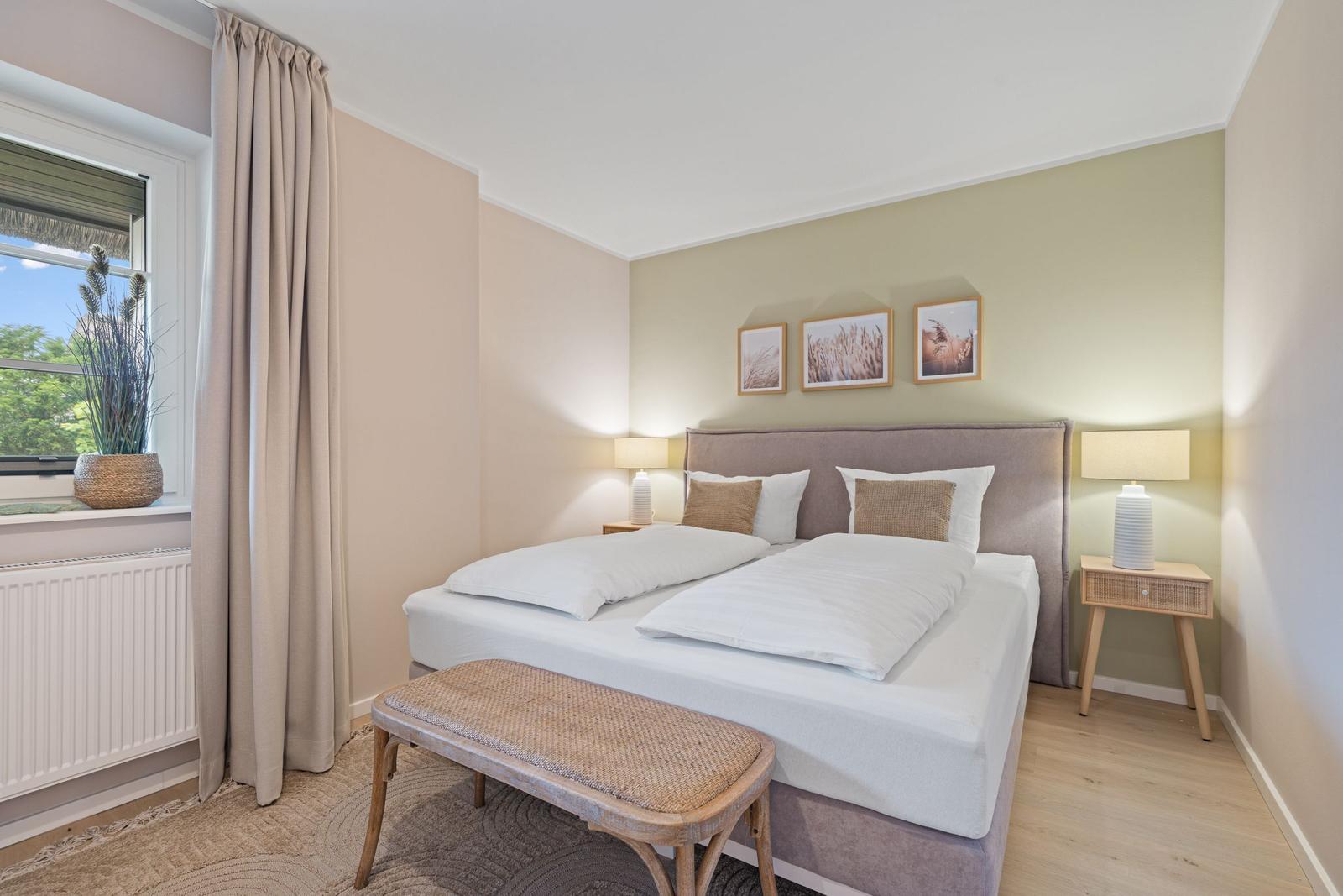 Schlafzimmer mit Doppelbett, zwei Nachttischen und Fenster mit Vorhang.