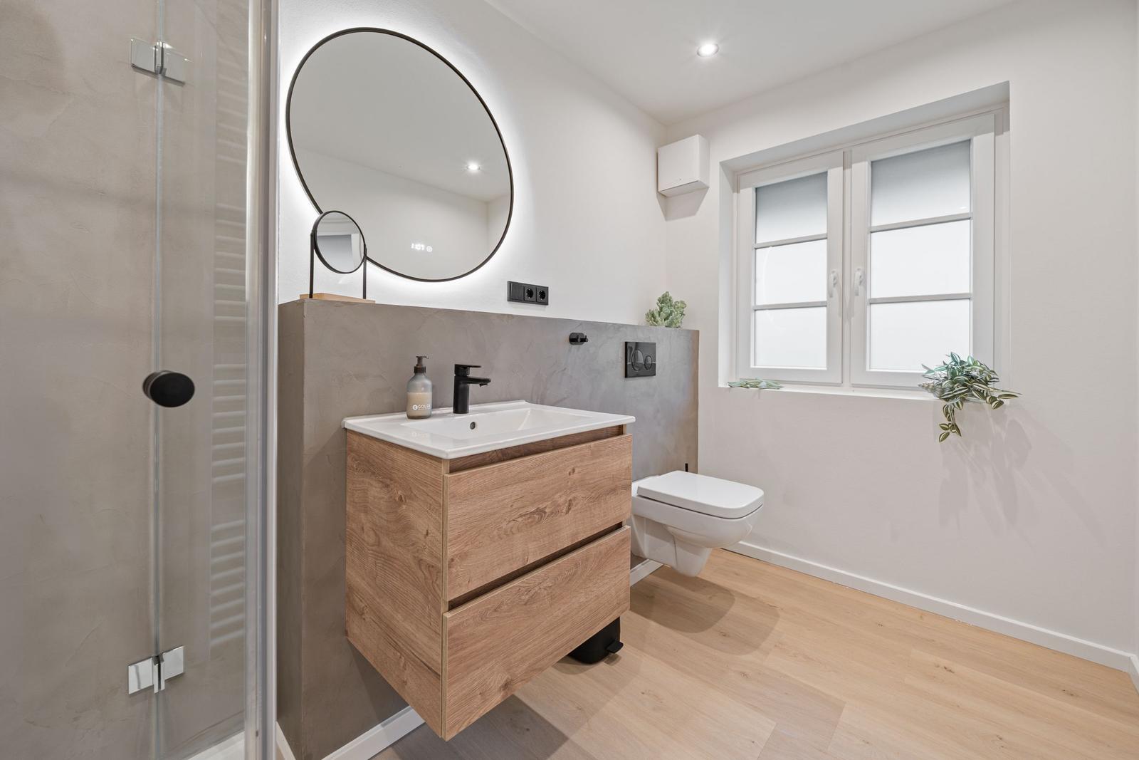 Badezimmer mit Waschbecken, Spiegel, Toilette und Dusche.