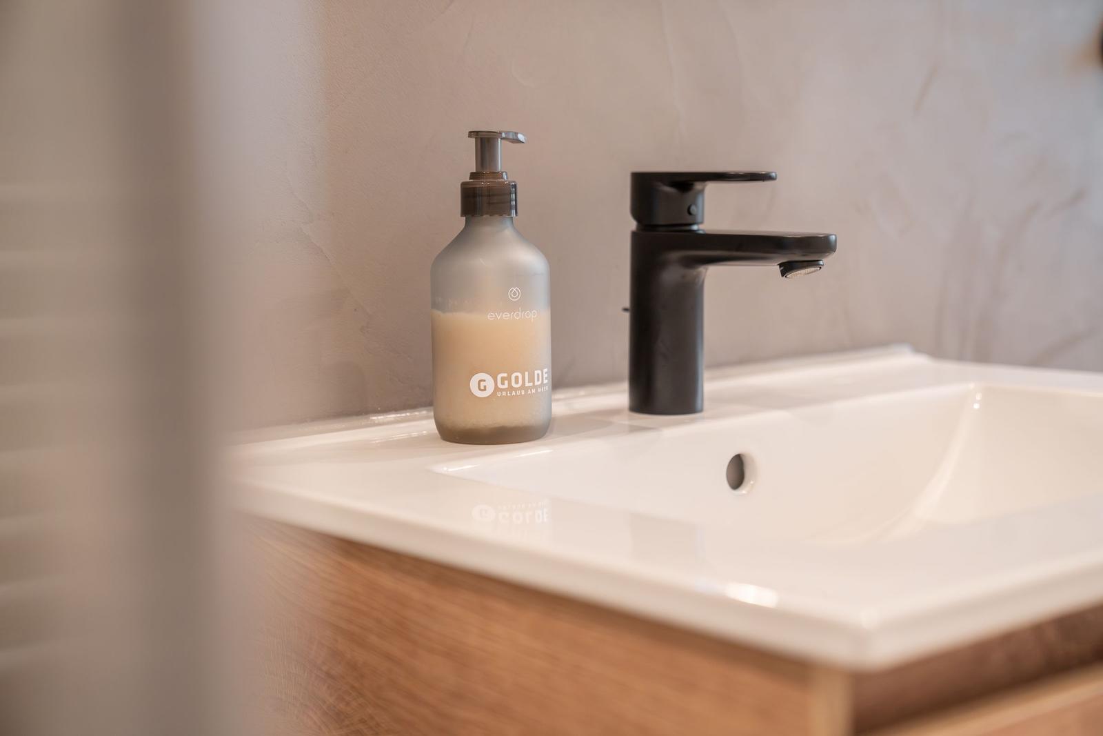 Waschbecken mit schwarzer Wasserhahn und Seifenspender auf Holzunterschrank