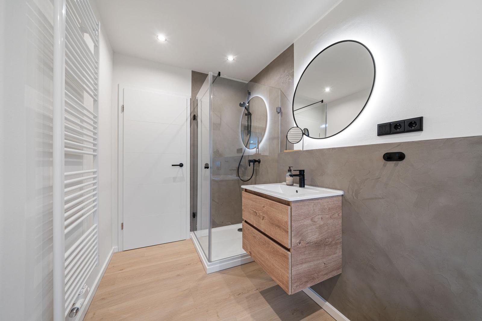 Badezimmer mit Dusche, Waschbecken und runden Spiegel.
