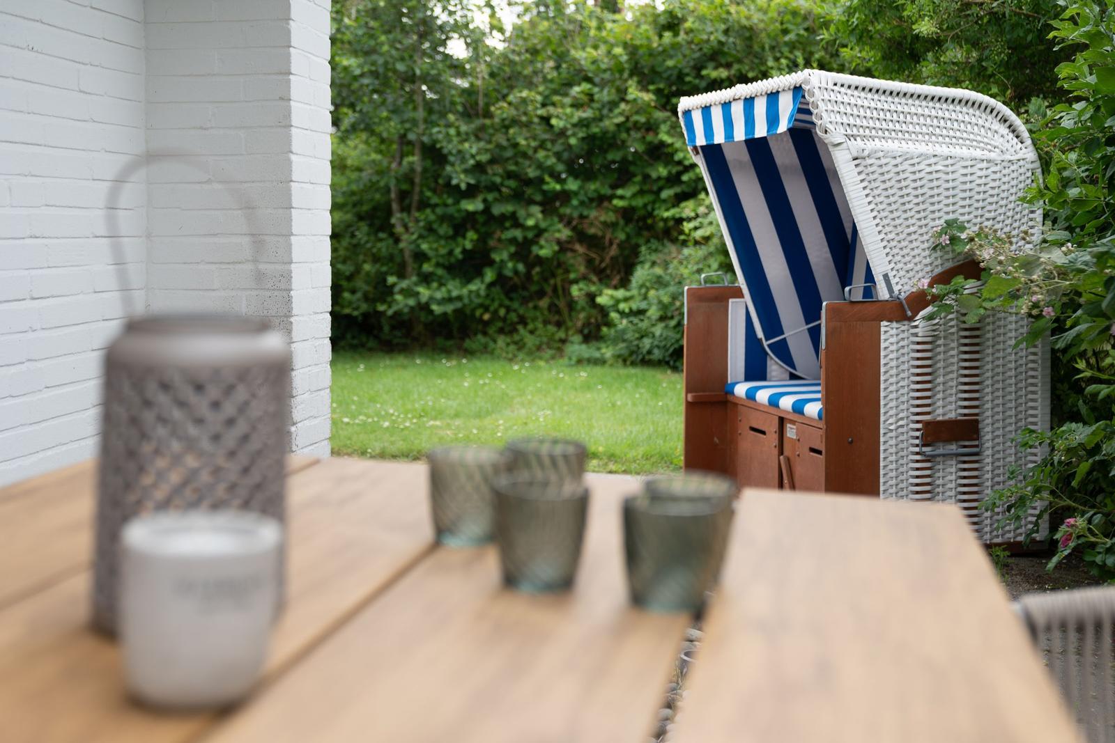 Terrasse mit Holztisch, Strandkorb und Garten.