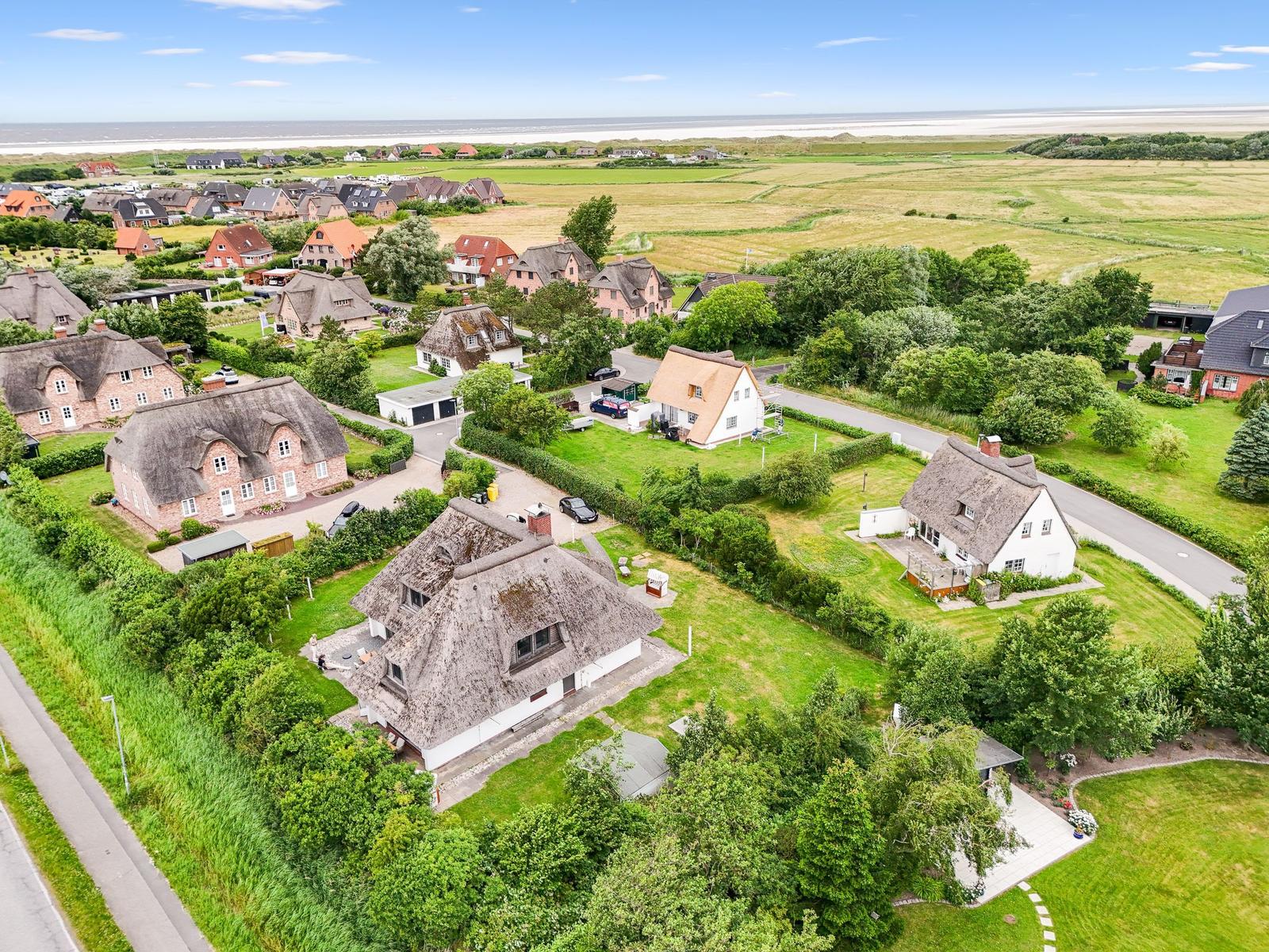 Dorf mit strohgedeckten Häusern und grünen Wiesen bis zum Strand.