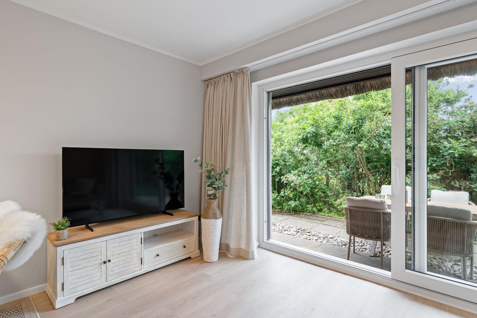 Wohnzimmer mit TV, Schiebetür zum Garten und Holzboden.