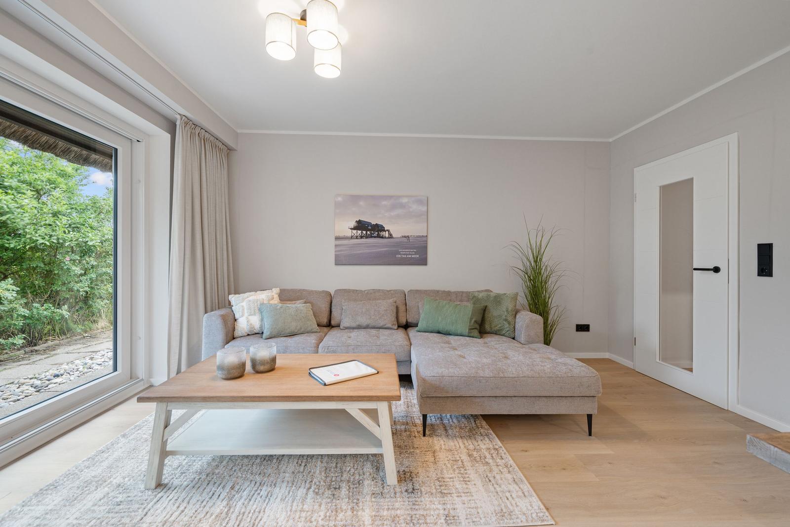 Wohnzimmer mit Sofa, Couchtisch und großem Fenster. Wandbild und Pflanze sichtbar.