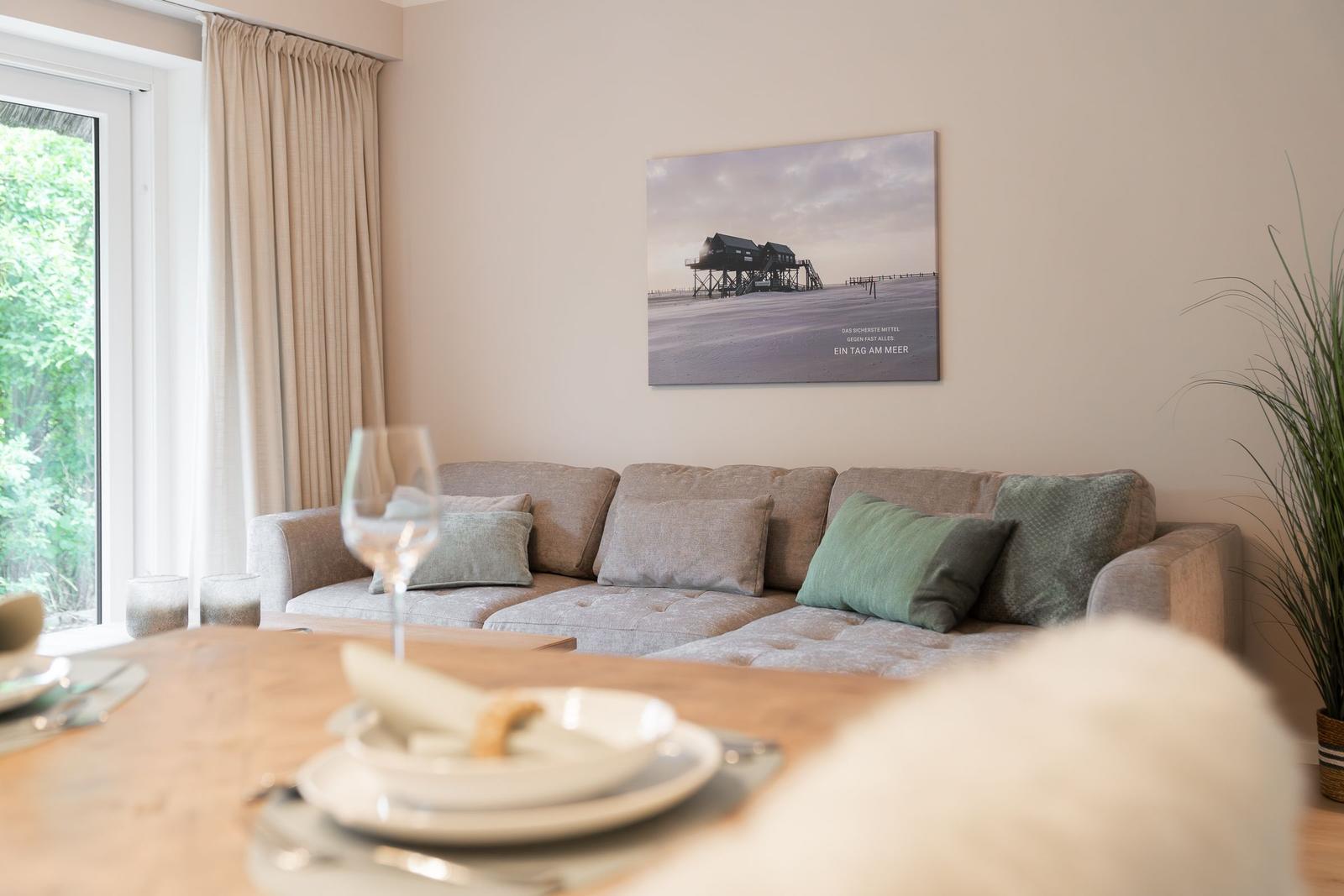 Wohnzimmer mit Sofa, Tisch und Wandbild. Fenster mit Vorhängen.