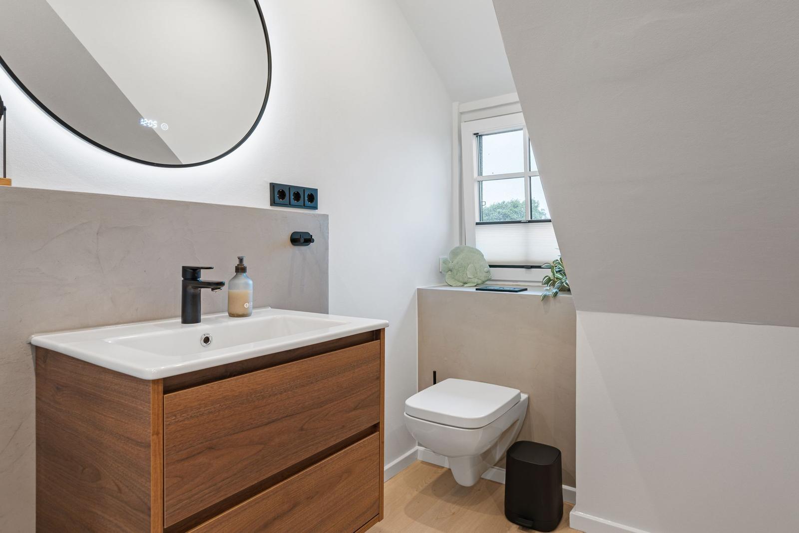 Badezimmer mit Waschbecken, Spiegel und Toilette unter Dachschrägen.