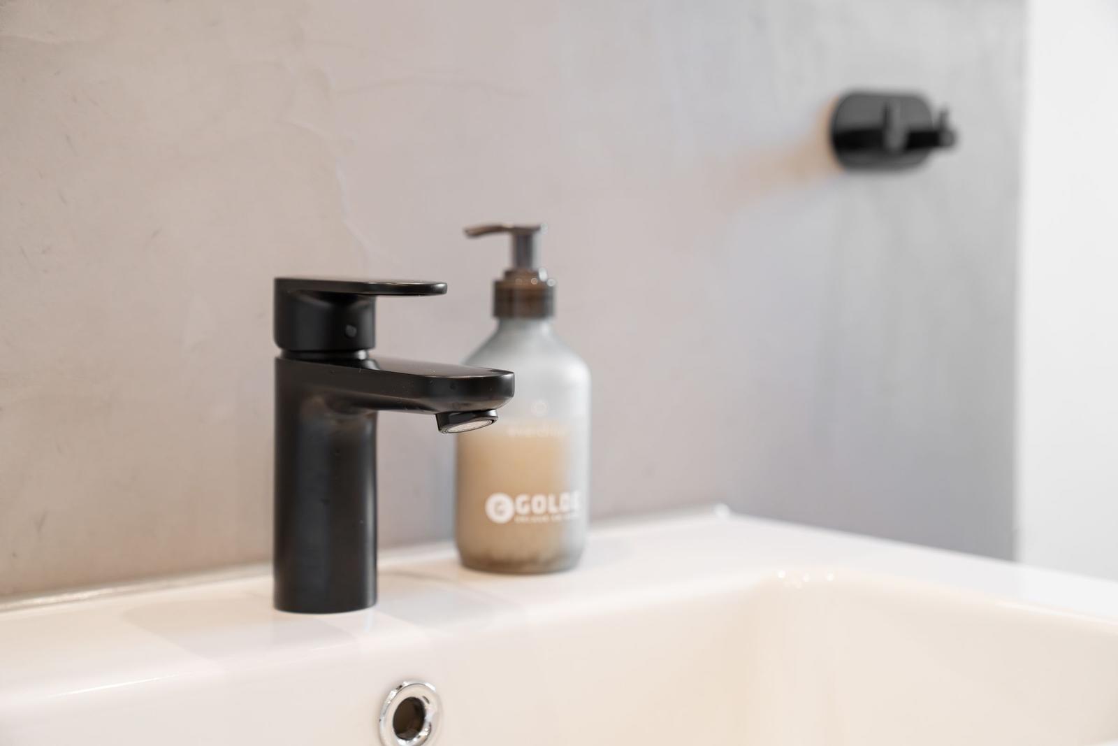 Schwarzer Wasserhahn auf weißem Waschbecken mit Seifenspender.