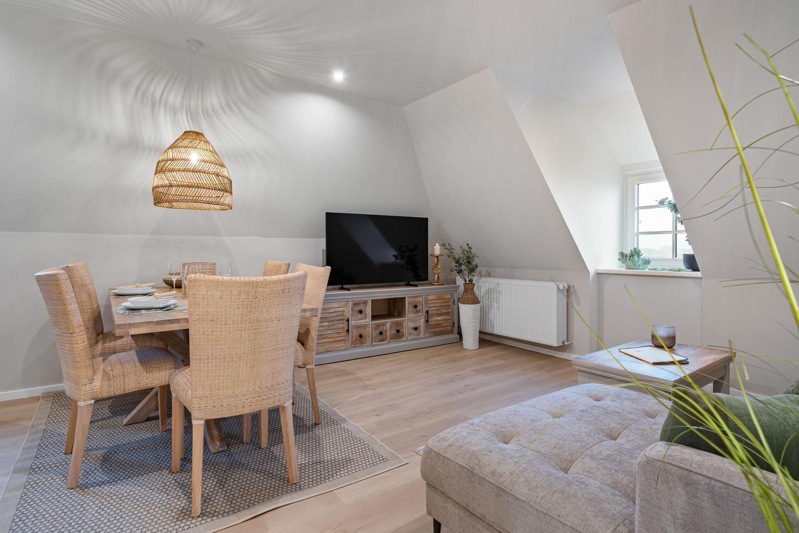 Wohn- und Essbereich mit TV, Esstisch und Sitzmöbeln unter schrägen Dachdecken.