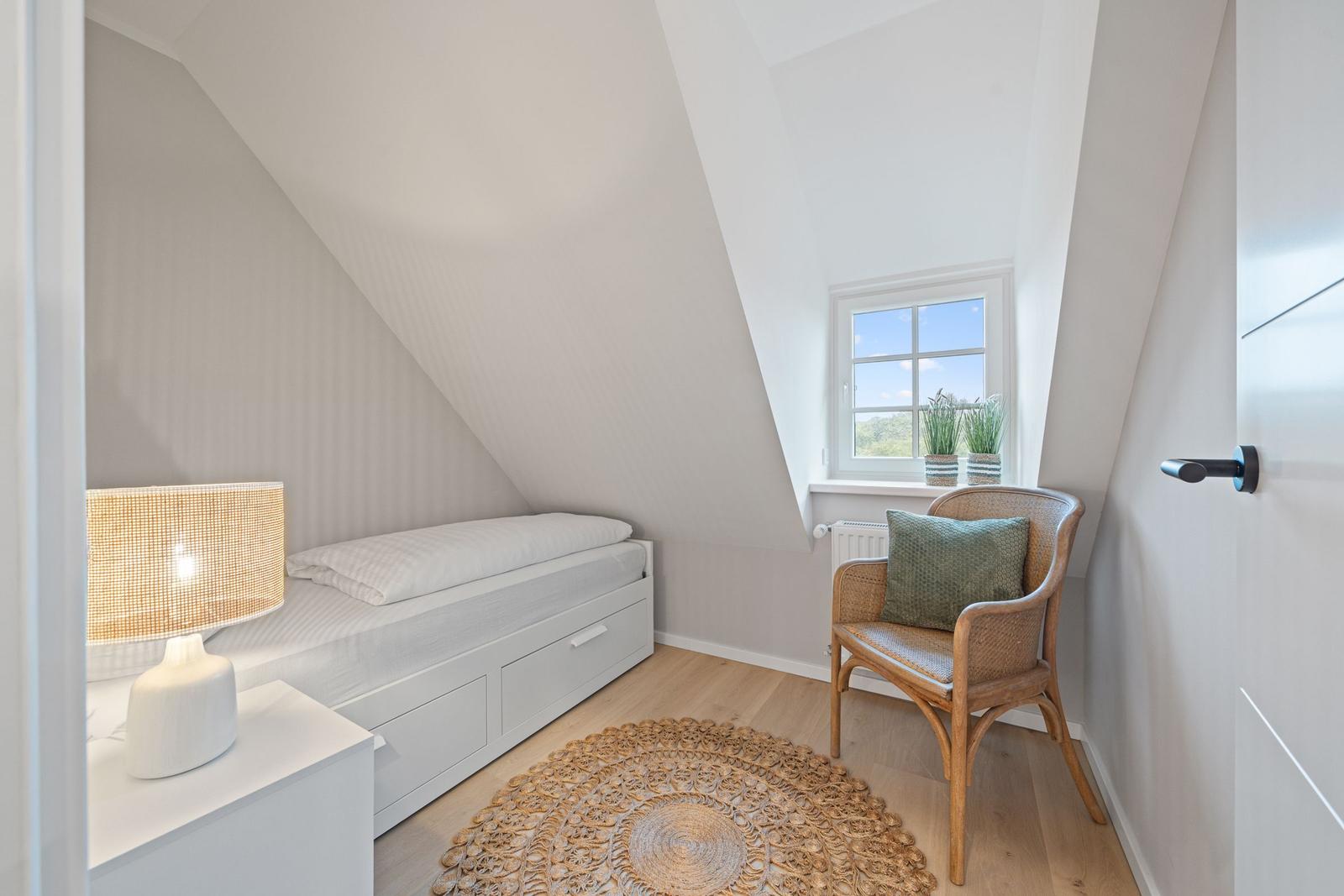 Schlafzimmer mit Dachschrägen, Bett, Stuhl und Fenster mit Blick.