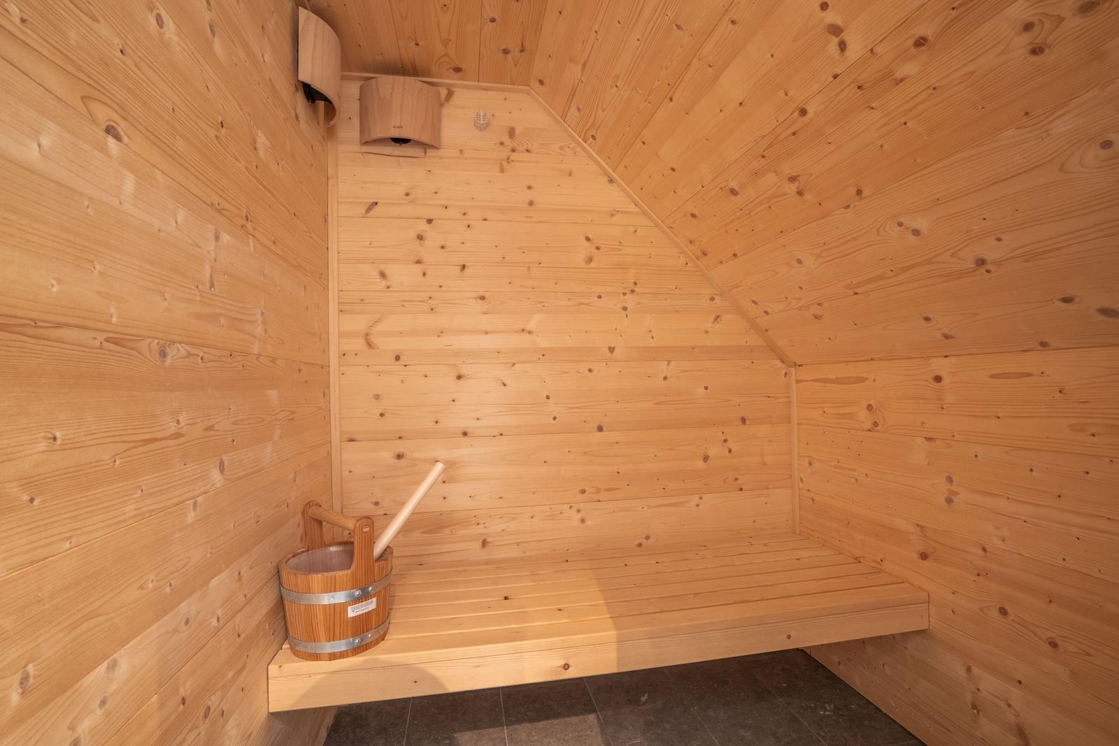 Sauna mit Holzbank und Eimer. Wände und Decke aus Holz.