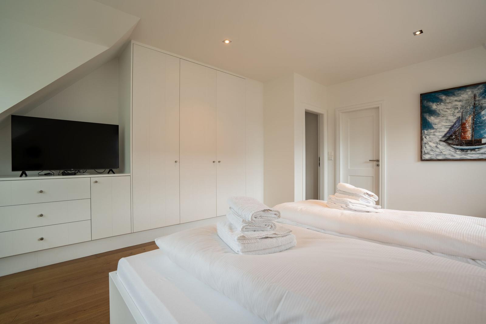 Zimmer mit zwei Betten, weißer Kleiderschrank und Fernseher an der Wand.