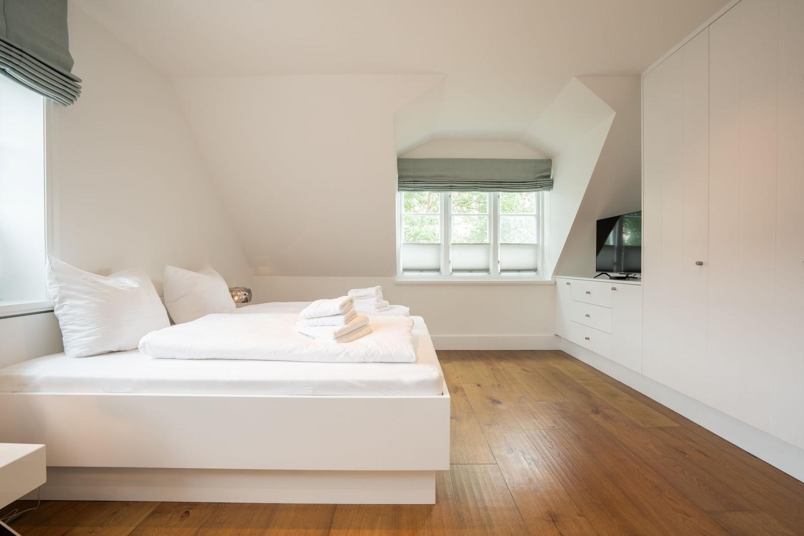Schlafzimmer mit weißem Bett, Holzboden und Fenster mit grünen Rollläden.