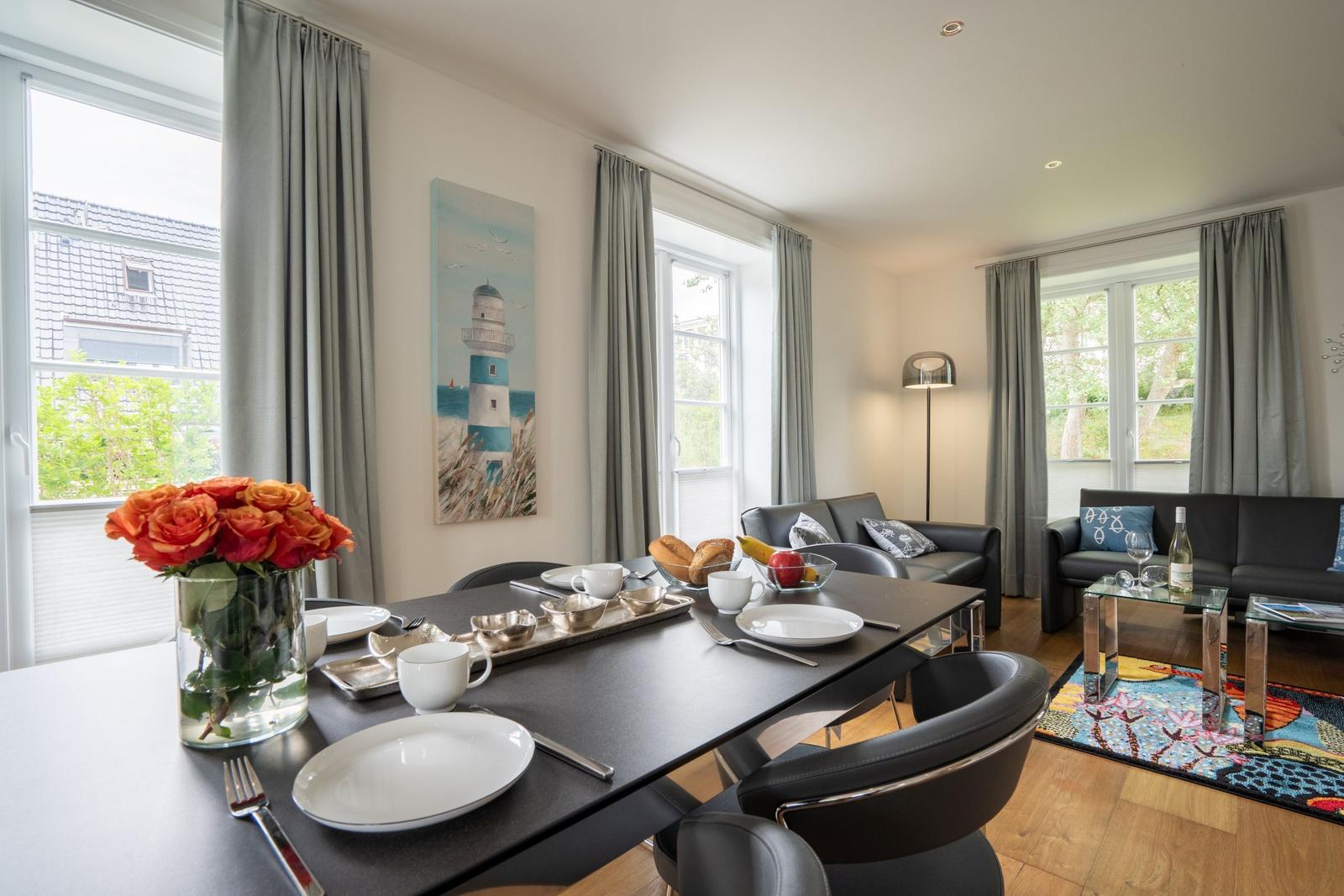 Esstisch mit Stühlen, Sofa, Fenster und Wandbild mit Leuchtturm.