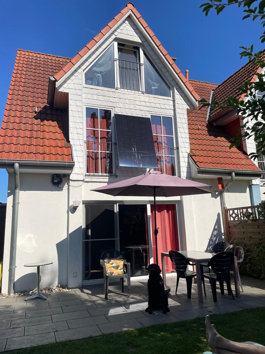 Haus mit Terrasse, Sonnenschirm und Garten. Ein Hund sitzt auf dem Boden.