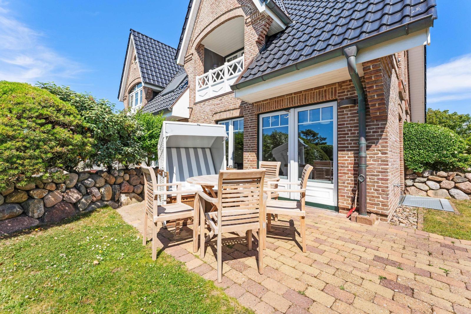 Terrasse mit Holztisch, Stühlen und Strandkorb vor Backsteinhaus mit Gartentor.