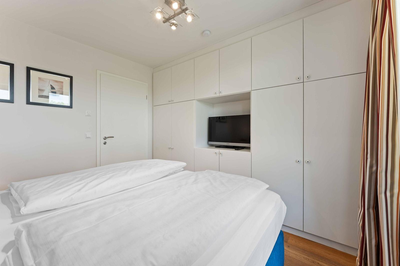 Bedroom with double bed, white wardrobes, and built-in TV.