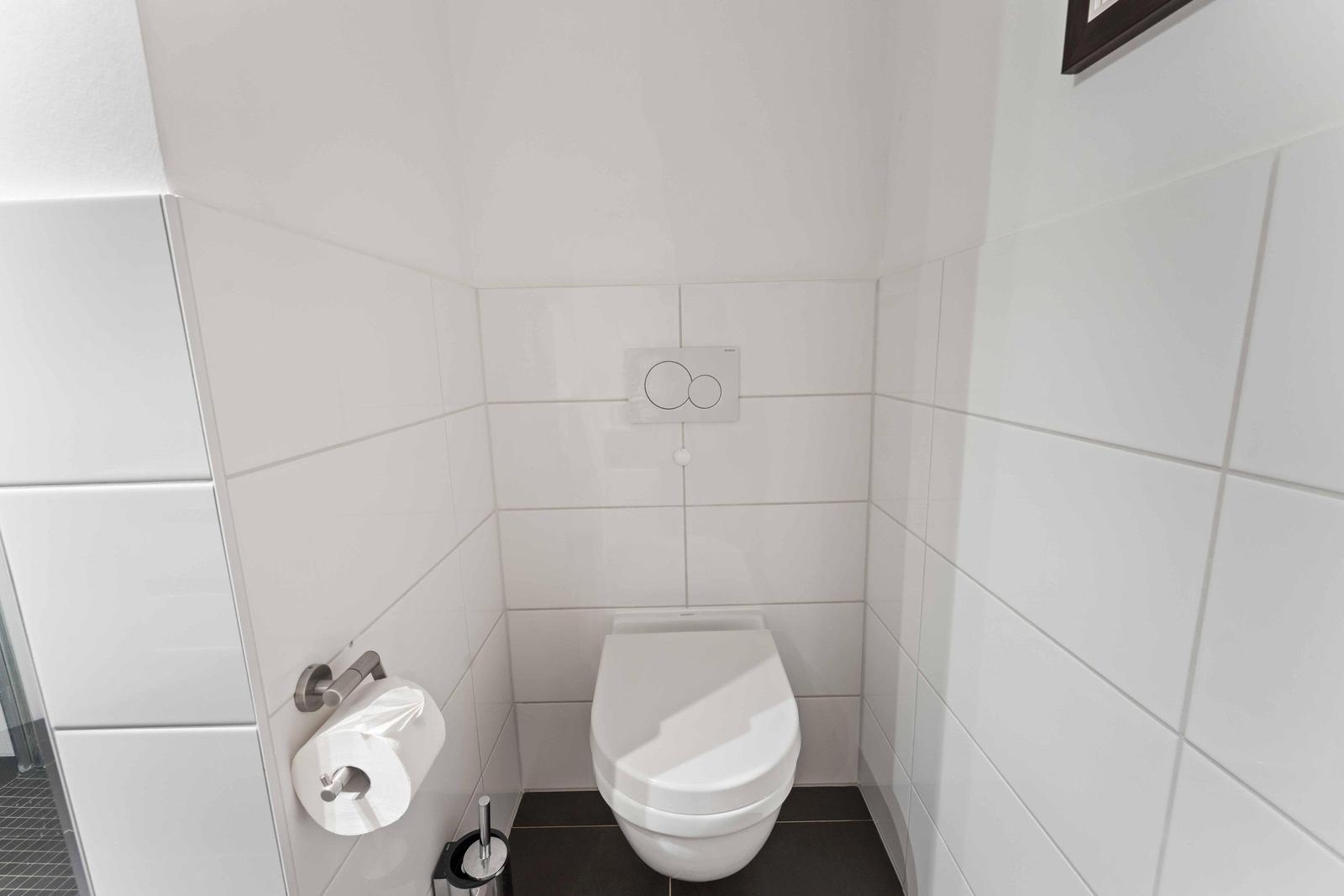 Toilet area with white wall tiles, toilet, and toilet paper holder.