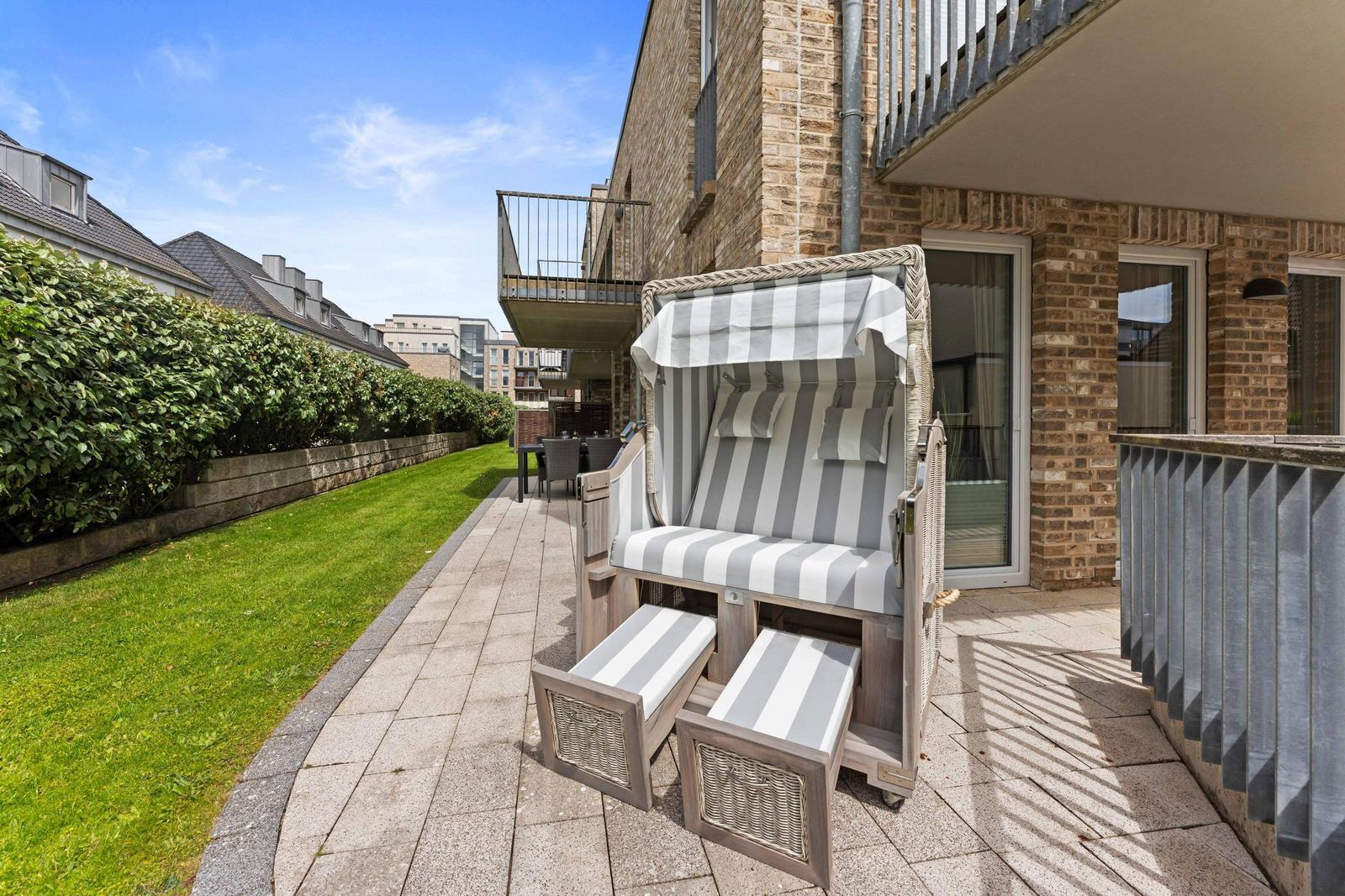 Terrace with beach chair, lawn, and balcony in background.