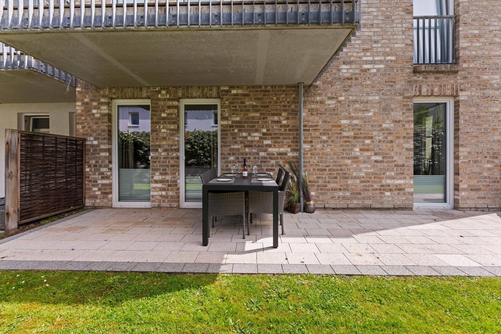 Terrace with table and chairs under a canopy. Background: brick wall and windows.