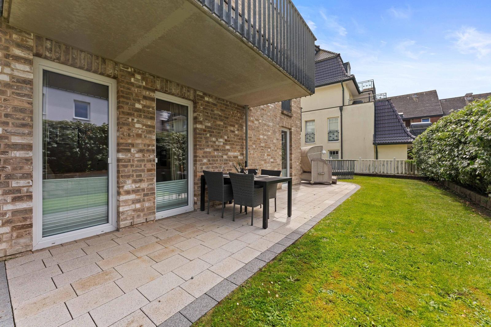Terrace with table and chairs beside green lawn area.