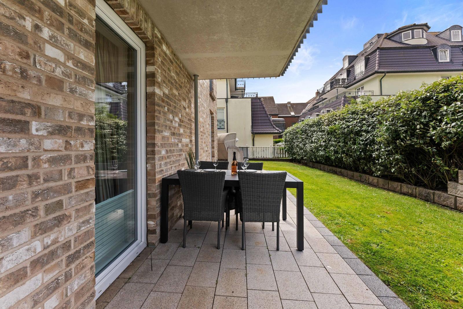 Terrace with table and chairs beside a glass front and green lawn.