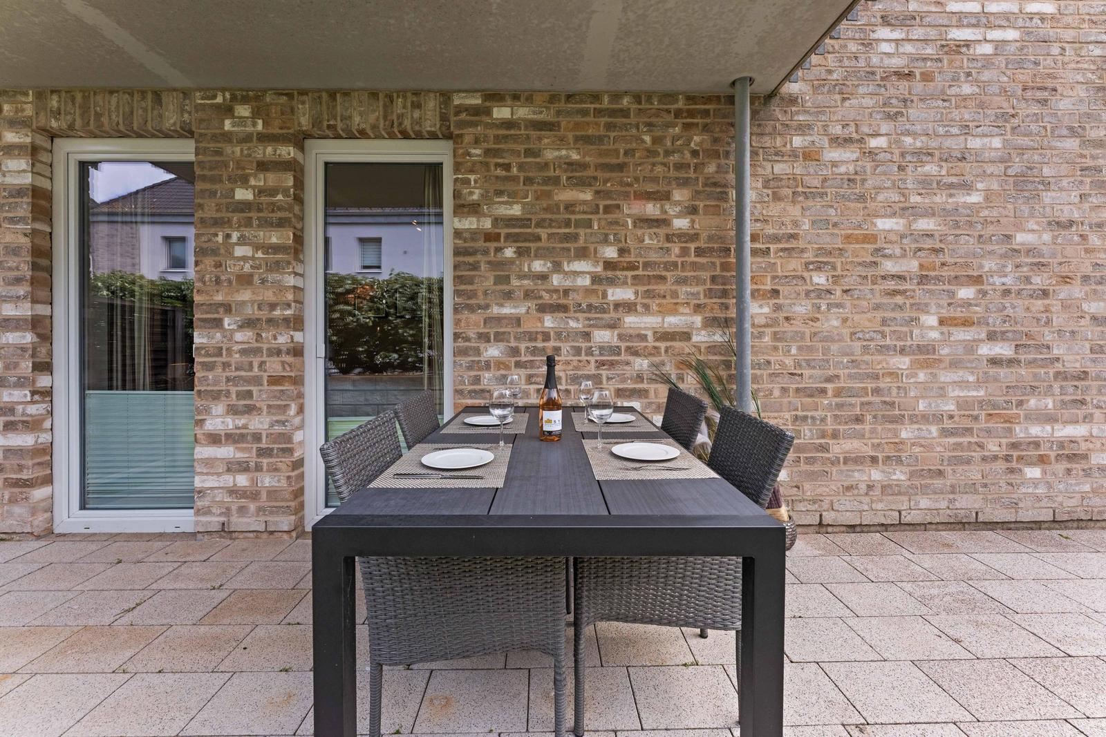 Terrace with set dining table and wine bottle against brick wall.