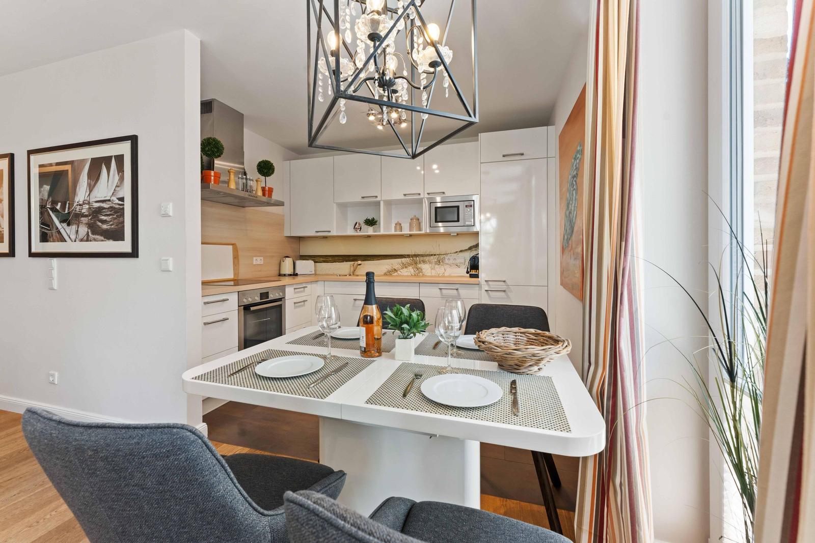 Dining area with table, chairs, and view into the kitchen. Ceiling light and window with curtains.