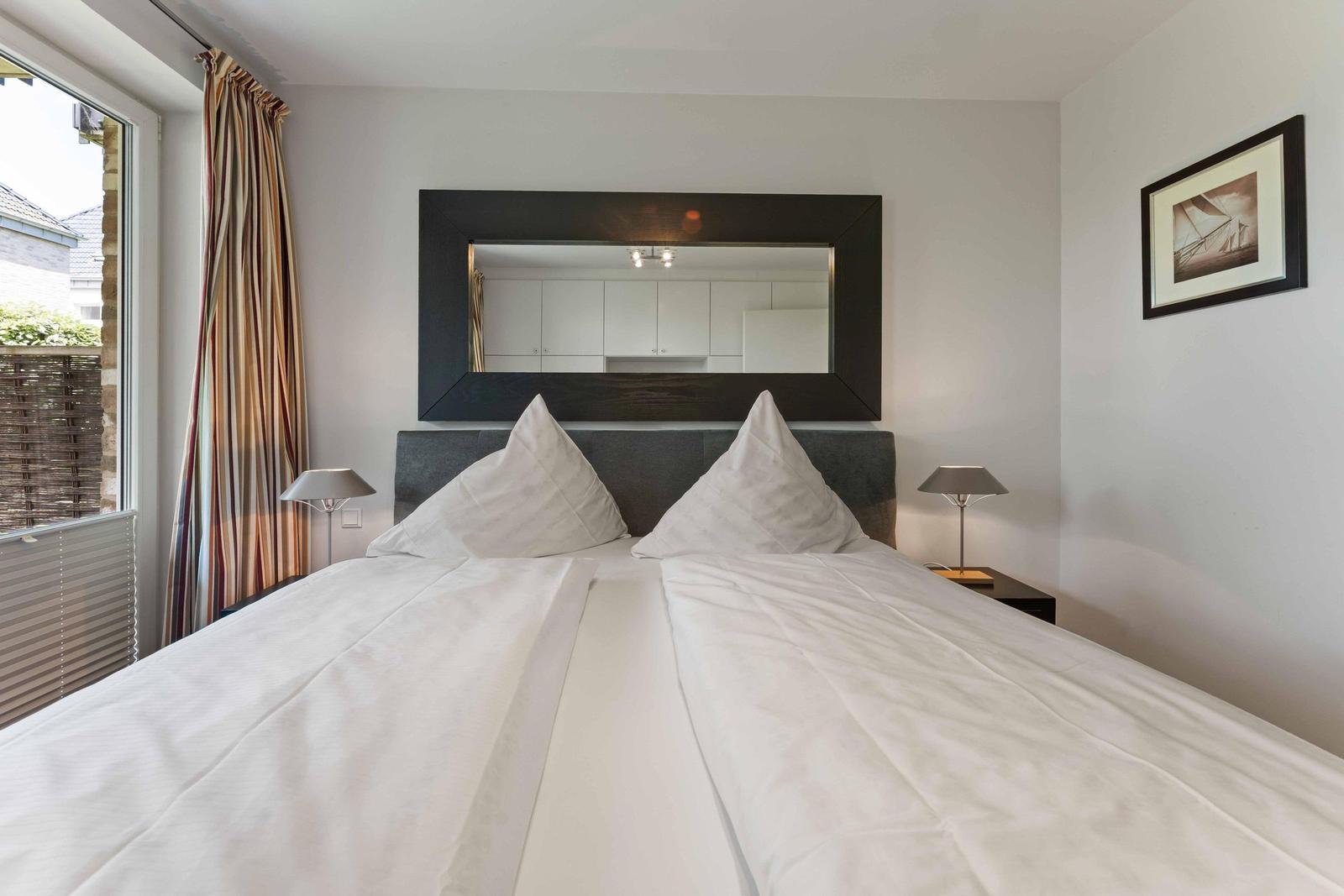 Bedroom with double bed, mirror, and window with curtain.
