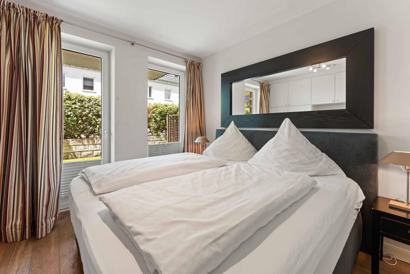 Bedroom with double bed, mirror cabinet, and windows overlooking the garden.