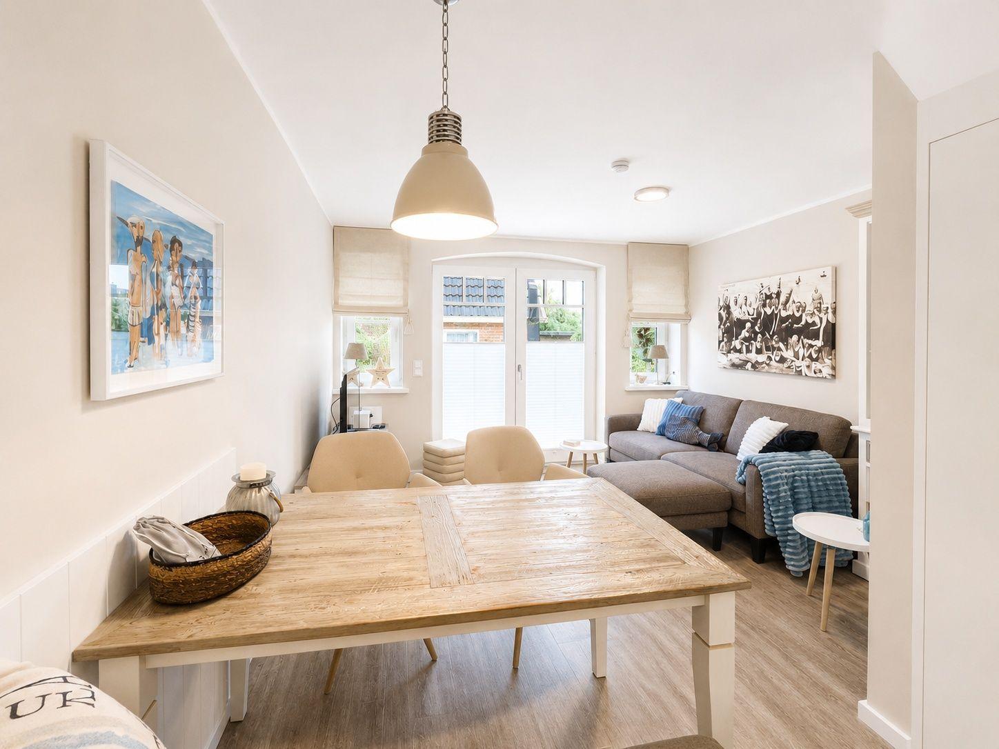 Essbereich mit Holztisch und Sitzgelegenheiten. Wohnbereich mit Sofa und Fenstern.