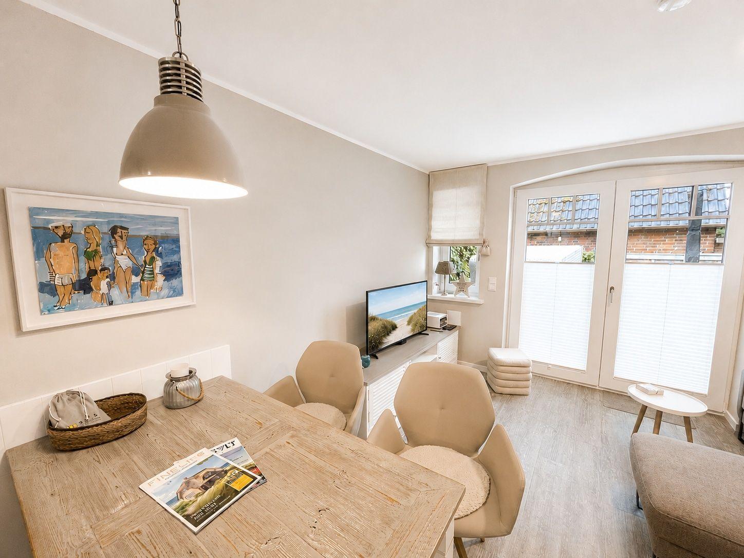 Essbereich mit Holztisch, Stühlen und Fernseher. Fenster mit Jalousien und Wandbild.