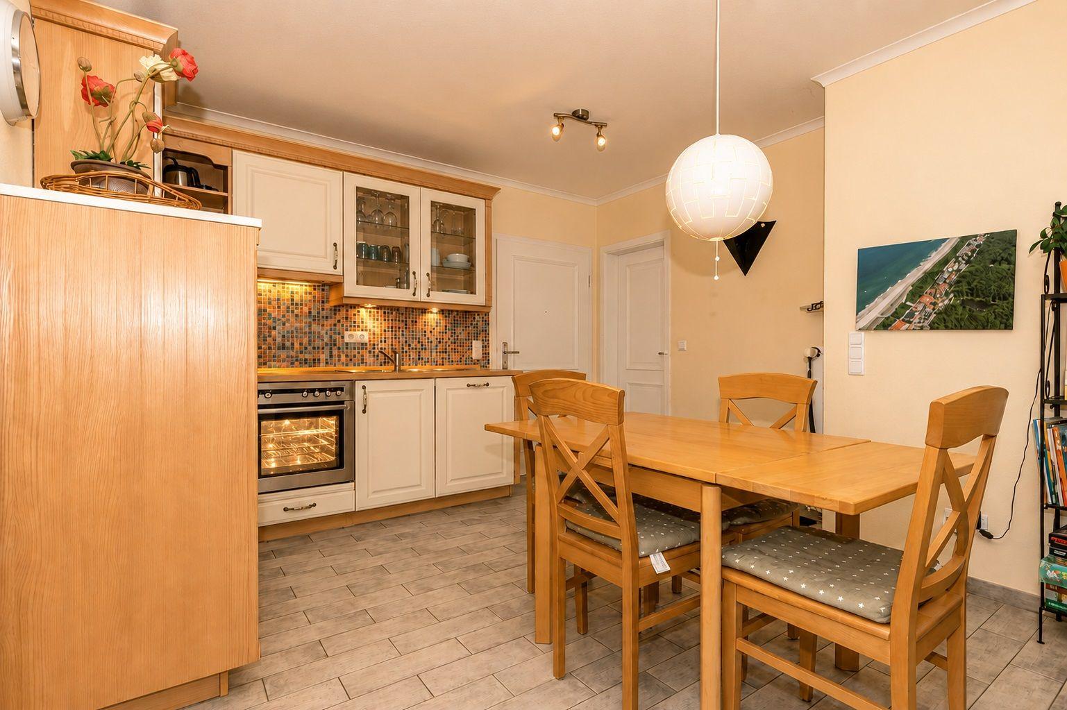 Küche mit Essbereich, Holztisch, Stühle und integrierte Kochgeräte.